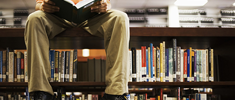 Man Reading Book and Sitting on Bookshelf in Library